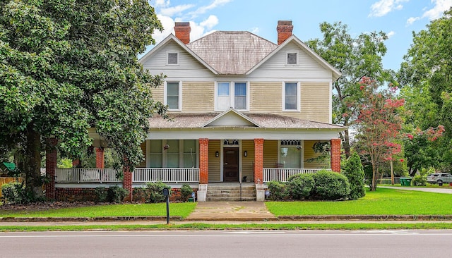 view of front of property with a porch, a chimney, and a front yard