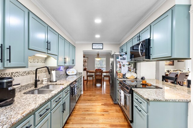kitchen with stainless steel appliances, a sink, ornamental molding, blue cabinetry, and light stone counters