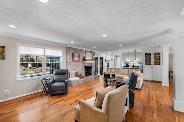living area featuring a textured ceiling, ornamental molding, light wood-style flooring, a brick fireplace, and baseboards