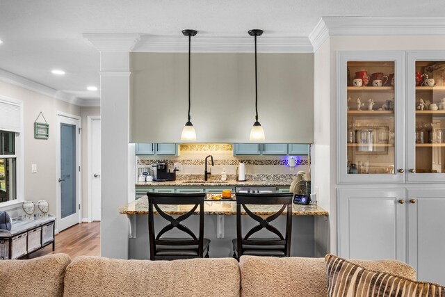 kitchen featuring a sink, a kitchen breakfast bar, crown molding, light stone countertops, and backsplash