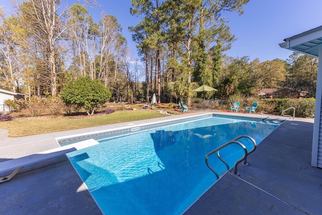 view of swimming pool featuring a diving board, a patio, and view of wooded area