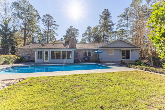 back of property with a lawn, a chimney, an outdoor pool, and a patio