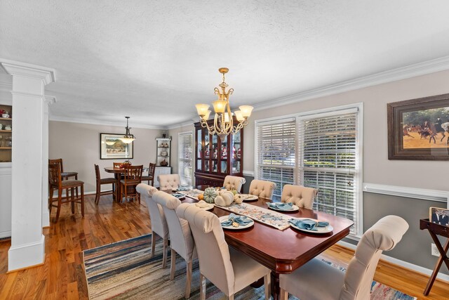dining area with ornate columns, wood finished floors, crown molding, a chandelier, and a textured ceiling