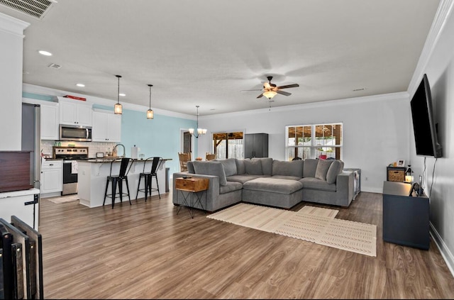 living room featuring dark wood-type flooring, ceiling fan with notable chandelier, and ornamental molding