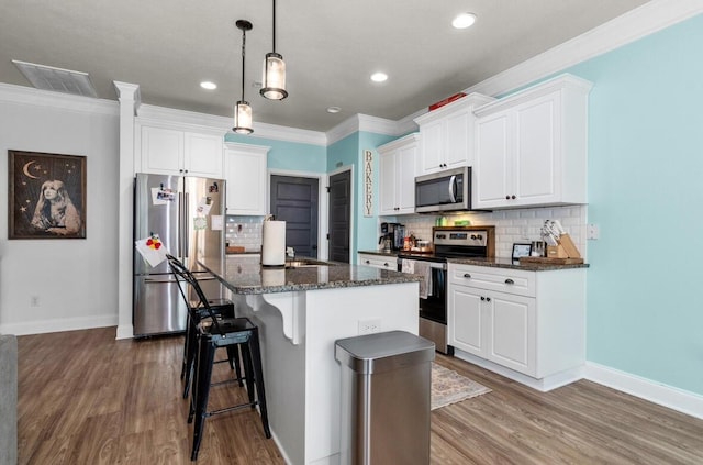 kitchen with tasteful backsplash, stainless steel appliances, a kitchen island with sink, white cabinets, and hanging light fixtures