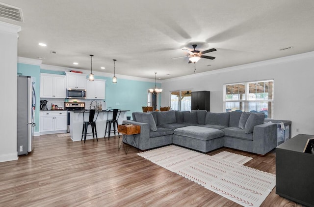 living room featuring hardwood / wood-style flooring, ceiling fan with notable chandelier, sink, and crown molding