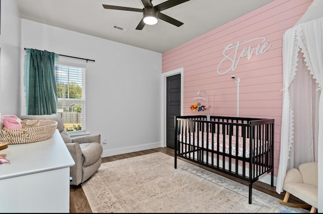 bedroom with ceiling fan, light wood-type flooring, and a crib