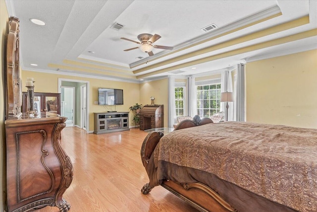 bedroom featuring ceiling fan, a raised ceiling, crown molding, light hardwood / wood-style floors, and a textured ceiling