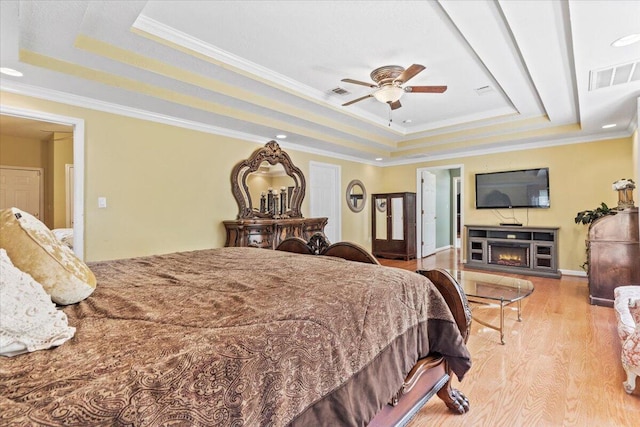 bedroom with a raised ceiling, ceiling fan, light wood-type flooring, and ornamental molding