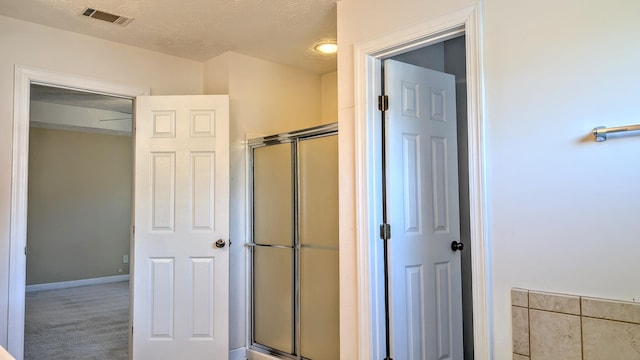 full bath featuring a textured ceiling, a shower with door, visible vents, and baseboards