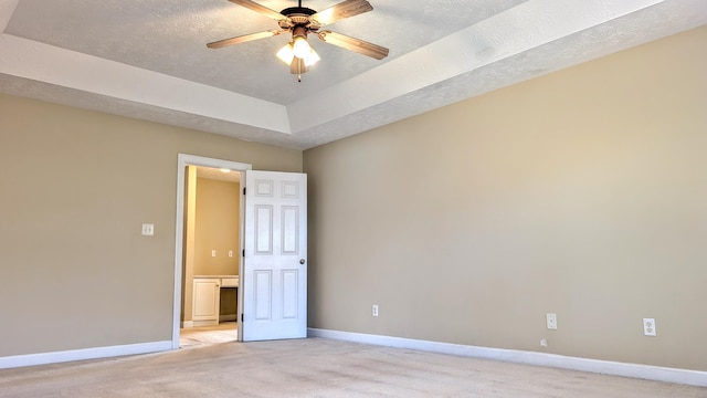 spare room featuring baseboards, a raised ceiling, a ceiling fan, and light colored carpet