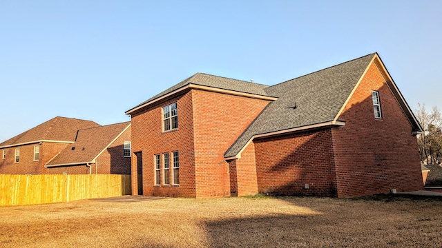 back of property featuring brick siding, fence, and roof with shingles