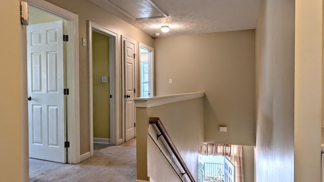 hall with a textured ceiling, baseboards, an upstairs landing, and light colored carpet