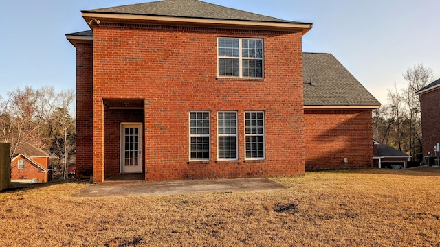 rear view of house with roof with shingles, a patio, a lawn, and brick siding