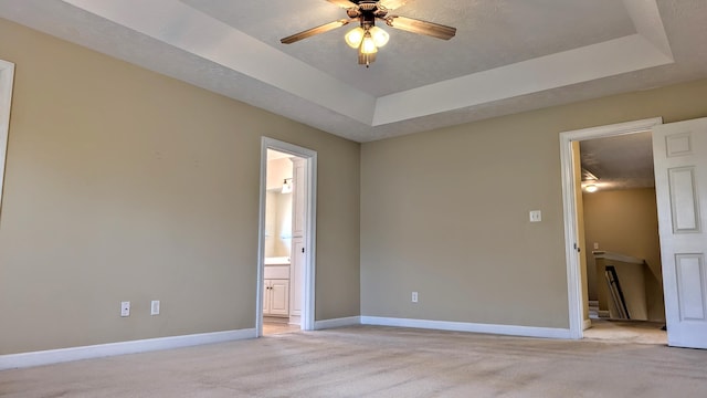 empty room with light carpet, a raised ceiling, and baseboards