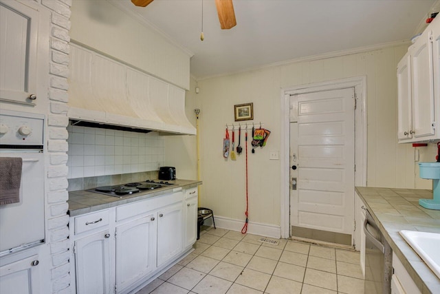 kitchen with cooktop, oven, tile counters, and crown molding