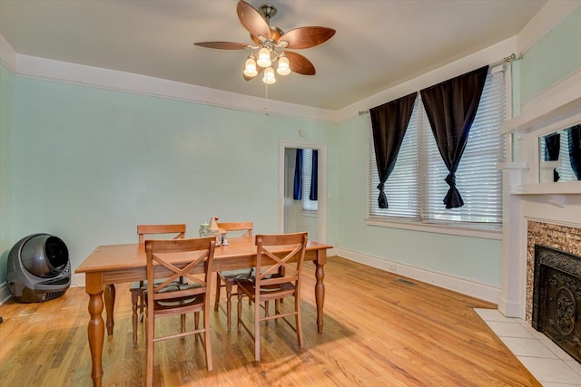 dining room with a tiled fireplace, ceiling fan, and light hardwood / wood-style flooring