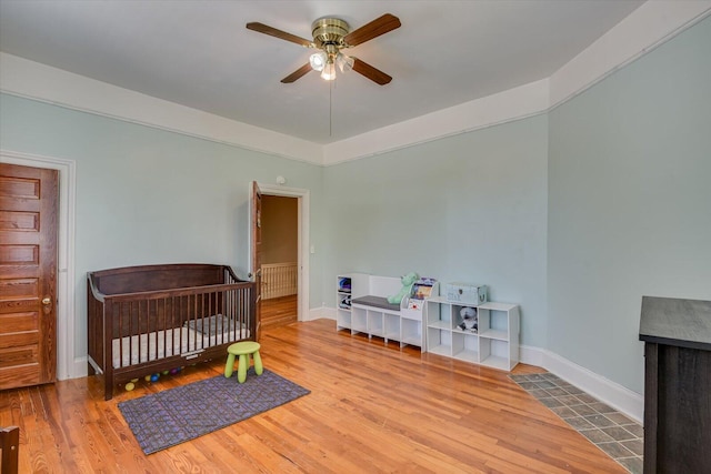 bedroom featuring wood-type flooring, a nursery area, and ceiling fan