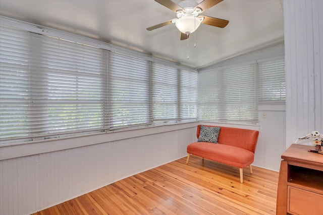 living area featuring wood-type flooring, ceiling fan, and wood walls