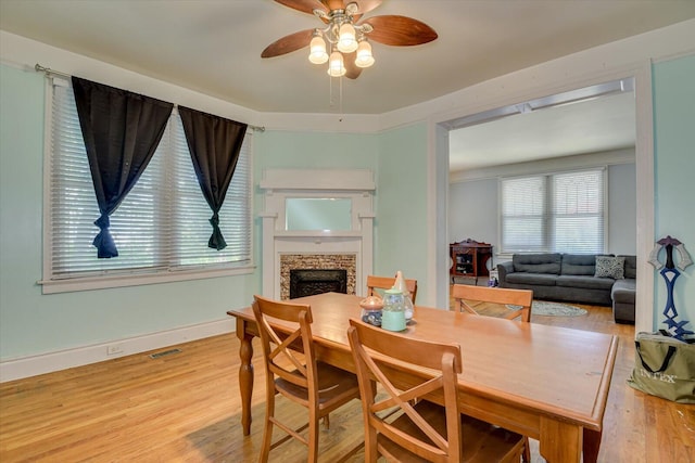 dining room with a fireplace, light hardwood / wood-style flooring, and ceiling fan