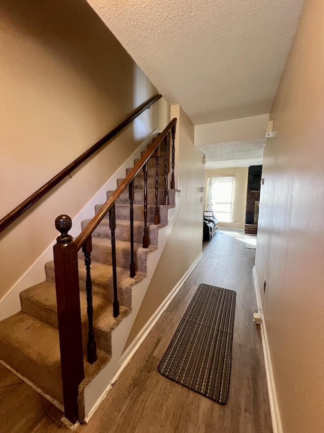 staircase featuring baseboards, a textured ceiling, wood finished floors, and a fireplace