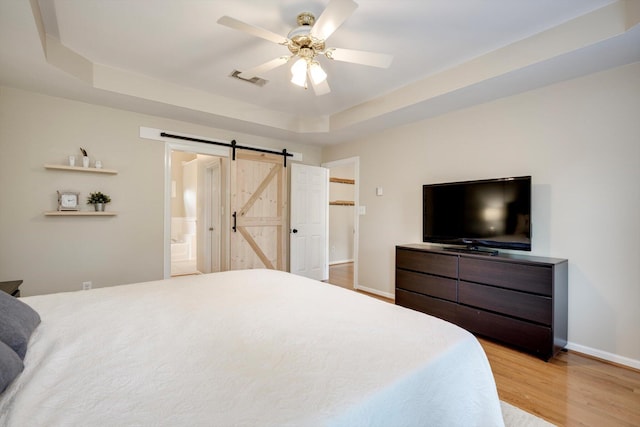225 Old Mill Rd, Martinez, GA 30907 - bedroom featuring a barn door, light wood-type flooring, ceiling fan, connected bathroom, and a tray ceiling