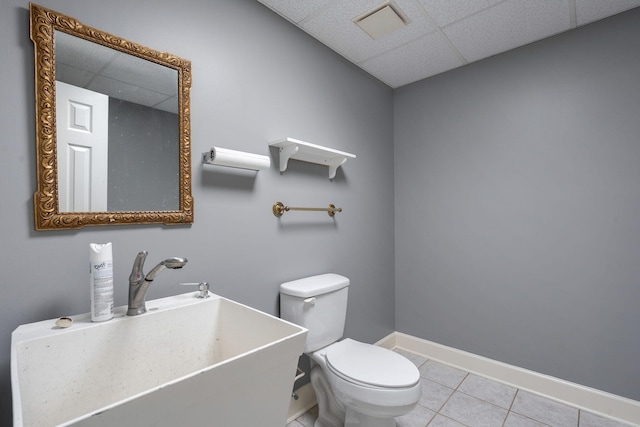 half bath featuring visible vents, a drop ceiling, toilet, tile patterned flooring, and a sink