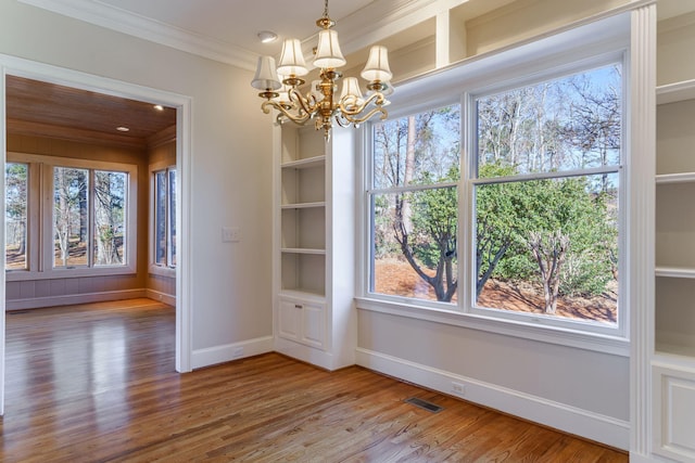 unfurnished dining area featuring a notable chandelier, crown molding, visible vents, wood finished floors, and baseboards