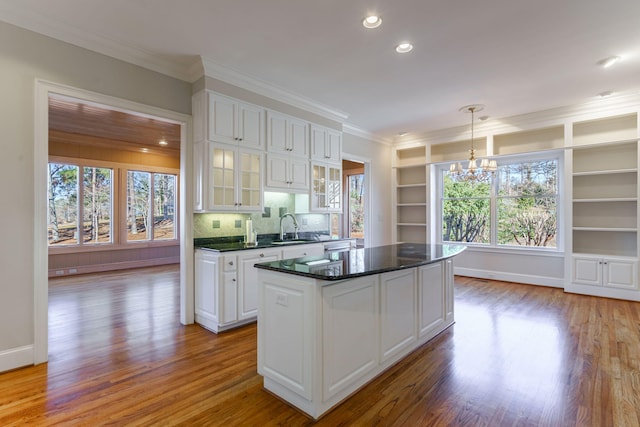 kitchen featuring a sink, a kitchen island, white cabinetry, hanging light fixtures, and glass insert cabinets