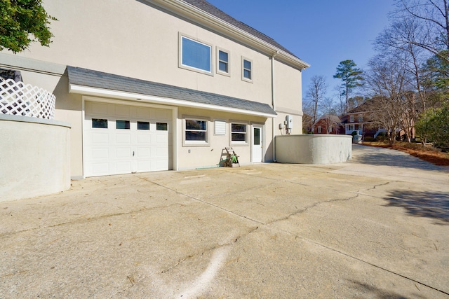 view of property exterior featuring roof with shingles, driveway, an attached garage, and stucco siding