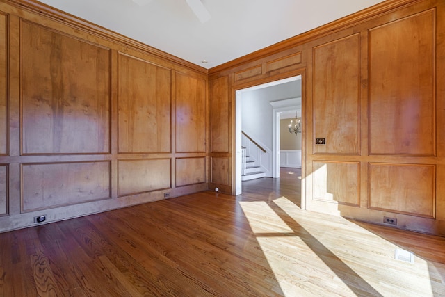 empty room featuring a notable chandelier, a decorative wall, visible vents, and wood finished floors