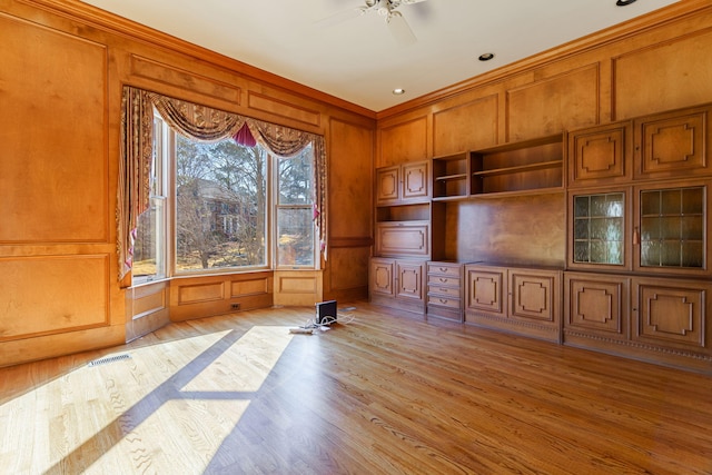 unfurnished living room with built in shelves, light wood-style flooring, and a decorative wall