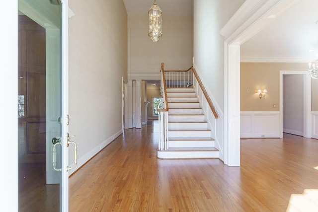 foyer featuring crown molding, an inviting chandelier, wainscoting, wood finished floors, and stairs