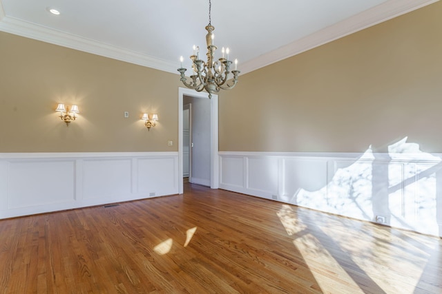 unfurnished room with visible vents, a wainscoted wall, ornamental molding, wood finished floors, and a notable chandelier