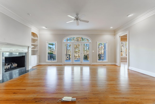 unfurnished living room featuring baseboards, crown molding, light wood-type flooring, built in shelves, and a fireplace