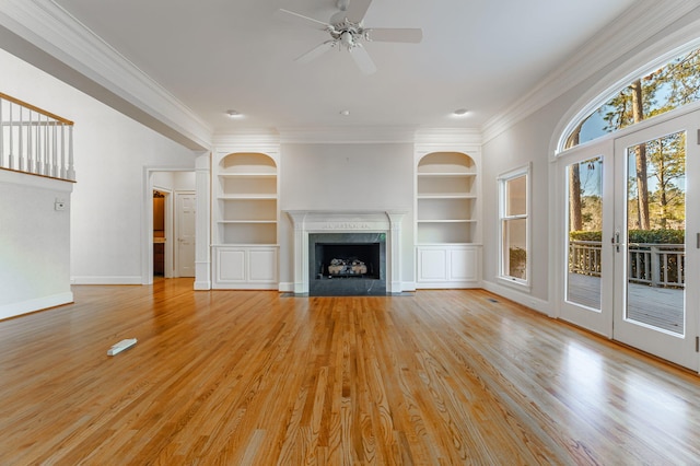 unfurnished living room with built in shelves, a healthy amount of sunlight, light wood-style flooring, and a premium fireplace