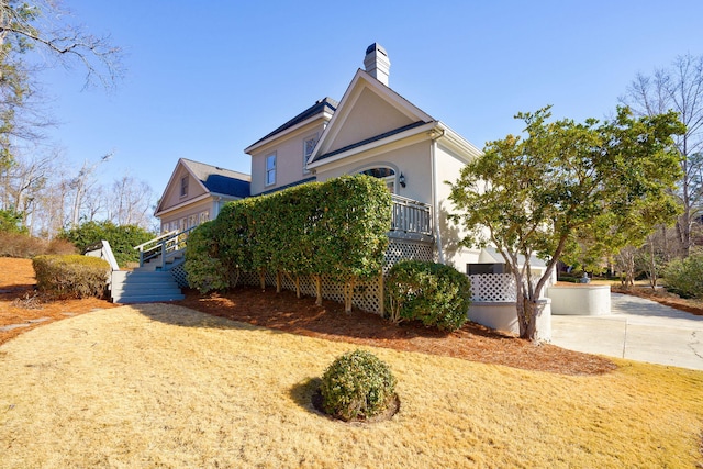 view of side of property with driveway, a chimney, and stucco siding