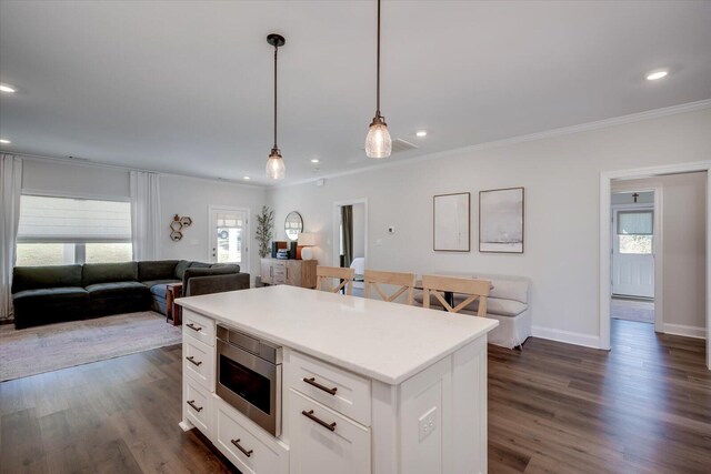 kitchen featuring white cabinetry, stainless steel microwave, a kitchen island, and pendant lighting