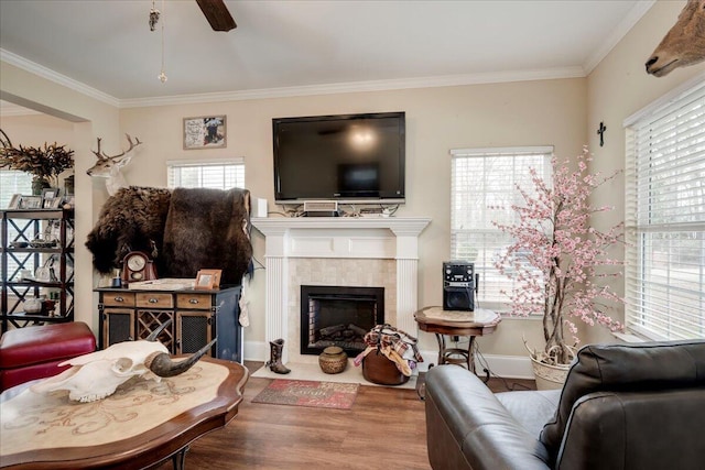 living room with hardwood / wood-style flooring, ceiling fan, ornamental molding, and a tiled fireplace