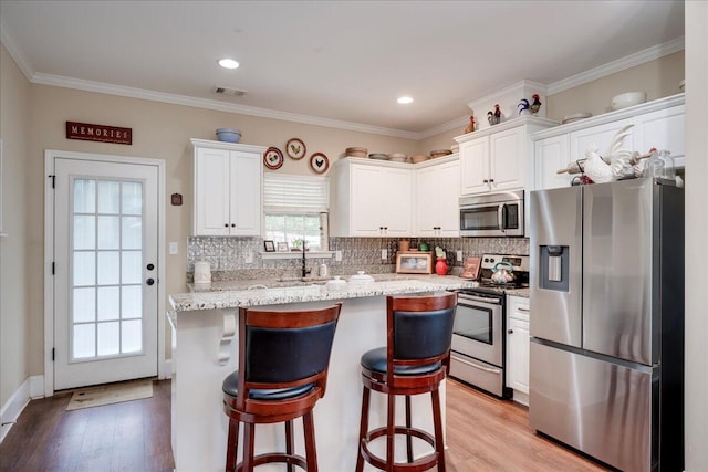 kitchen featuring decorative backsplash, appliances with stainless steel finishes, light stone countertops, light hardwood / wood-style flooring, and white cabinets