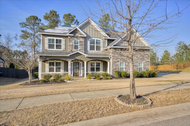 craftsman-style house featuring covered porch, stone siding, solar panels, and fence