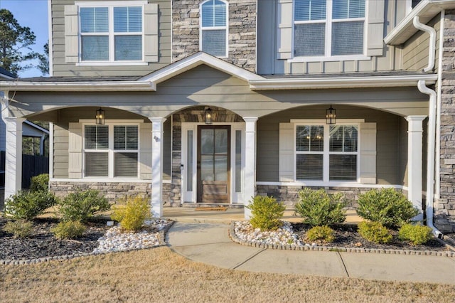 view of exterior entry with covered porch, stone siding, and board and batten siding