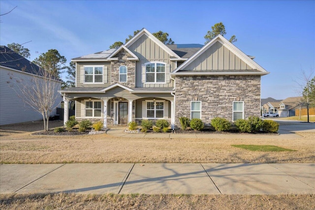 craftsman-style home featuring covered porch, stone siding, board and batten siding, and solar panels