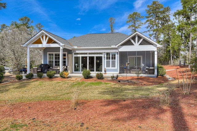 rear view of house with a sunroom, roof with shingles, a porch, and a yard