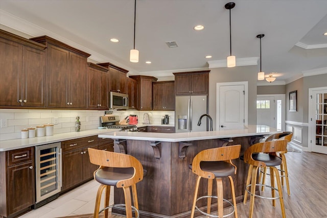 kitchen featuring crown molding, stainless steel appliances, light countertops, decorative backsplash, and beverage cooler