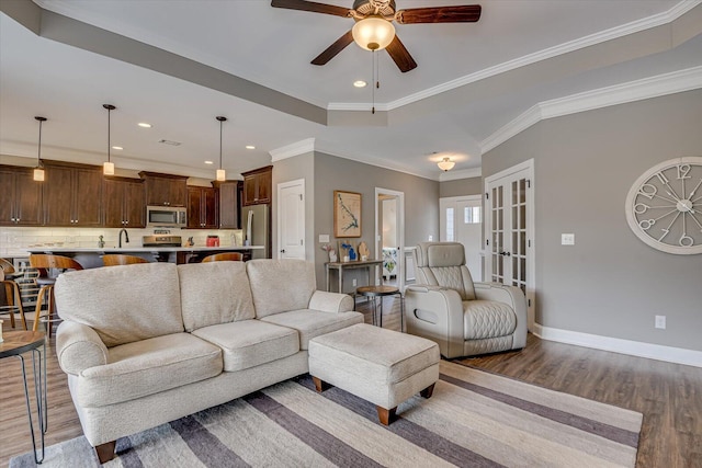 living room featuring crown molding, recessed lighting, a raised ceiling, wood finished floors, and baseboards