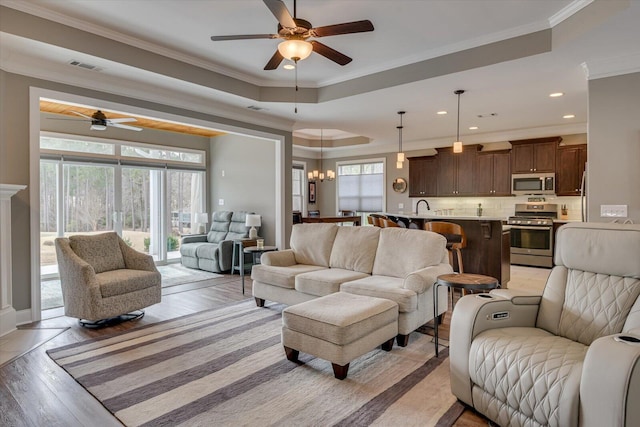 living room featuring ornamental molding, a raised ceiling, visible vents, and light wood-style floors