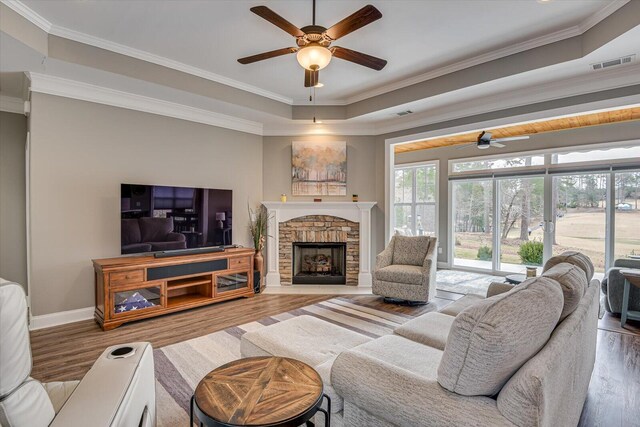 living room with baseboards, visible vents, wood finished floors, crown molding, and a stone fireplace