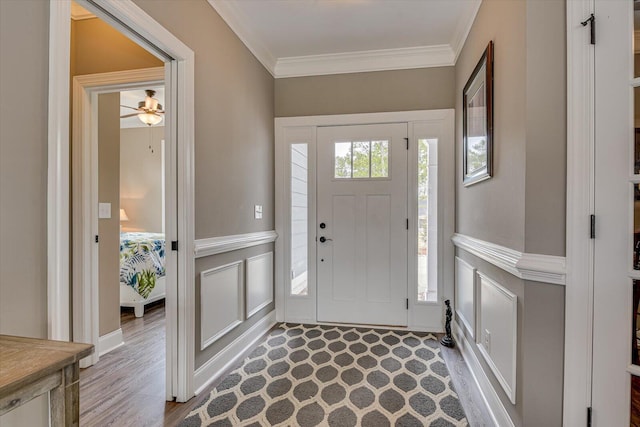 entryway with ornamental molding, wainscoting, and a decorative wall