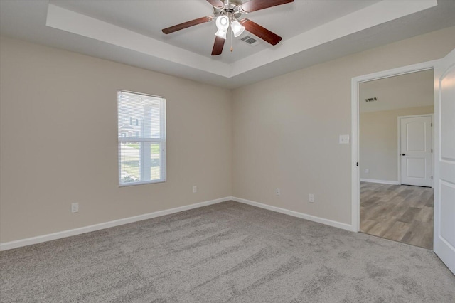 carpeted empty room with a raised ceiling and ceiling fan